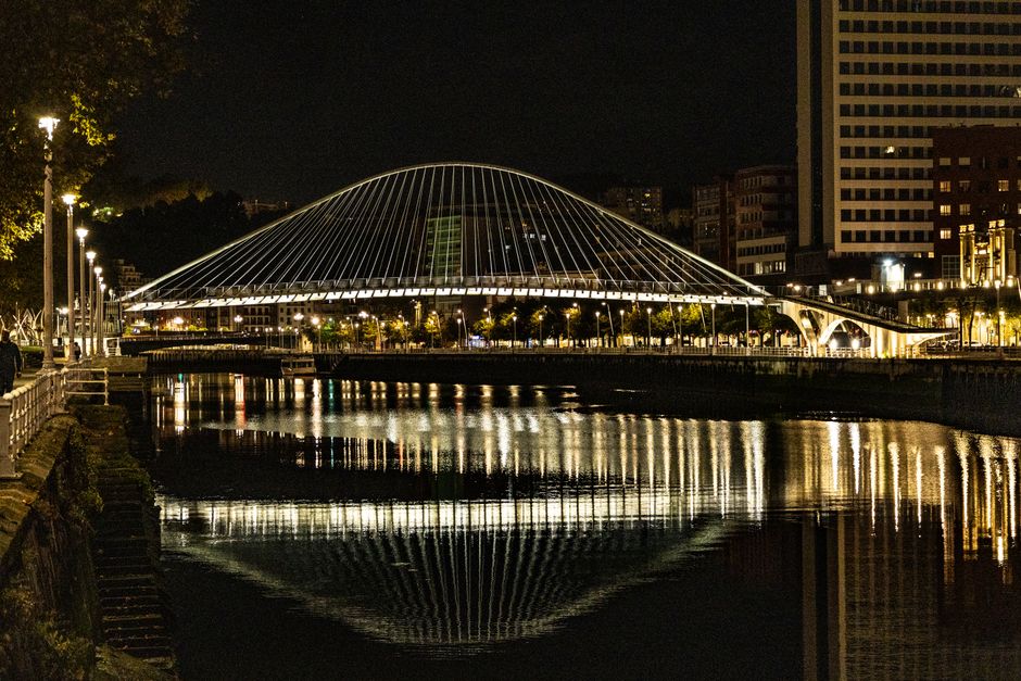 El puente Zubizuri de Bilbao iluminado, reflejado en la ría