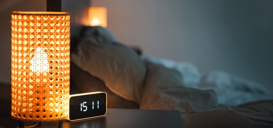 Lámpara encendida y reloj digital en una mesilla de noche, imagen del chat de cornudos hispano y sus horas cruzadas