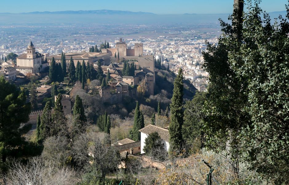La Alhambra sobre su colina, rodeada de cipreses, con la ciudad de Granada y la vega al fondo.