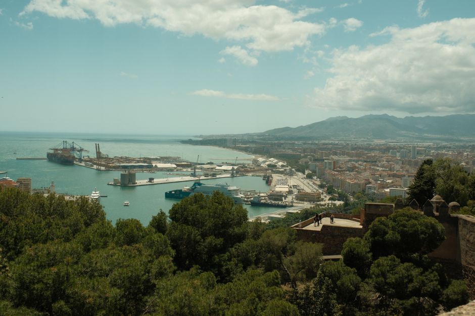 El puerto de Málaga y la costa vistos desde lo alto, con los montes al fondo y la ciudad extendiéndose hacia el este.
