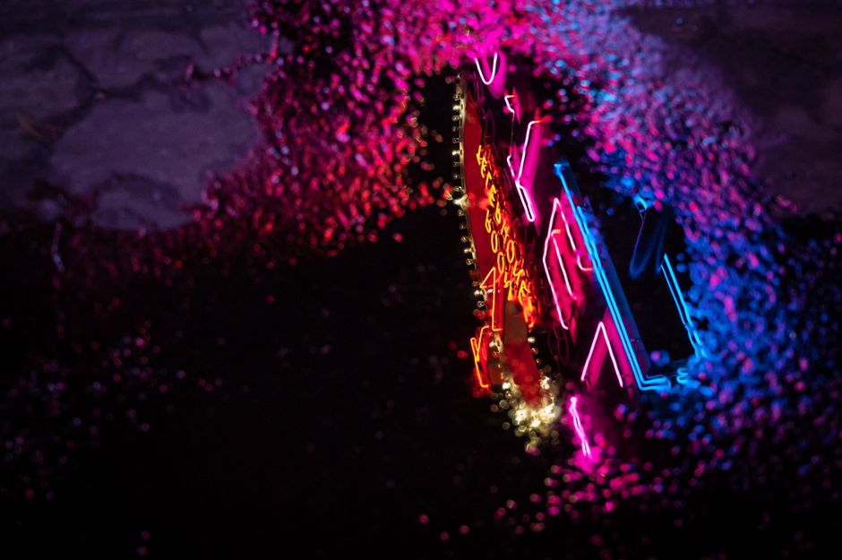 Neón rosa y azul reflejado en un charco, en una calle de noche bajo la lluvia