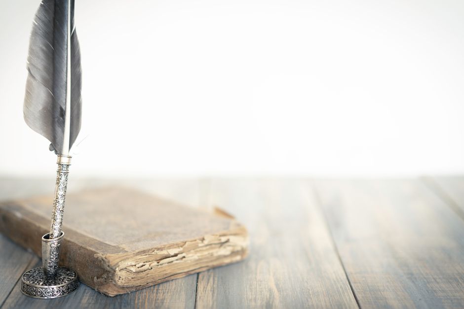 Pluma de ave junto a un libro envejecido sobre una mesa de madera
