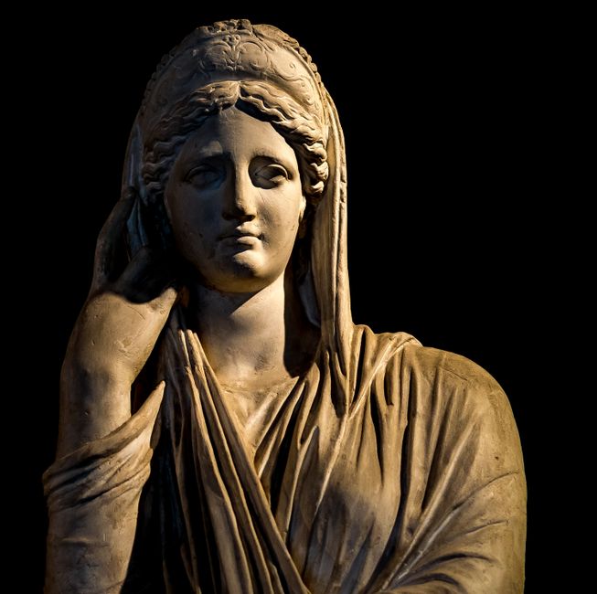 Estatua de piedra con los pliegues del ropaje tallados, a contraluz
