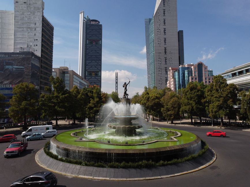 México: Scenic view of a roundabout featuring a central fountain surrounded by skyscrapers on a sunny day.